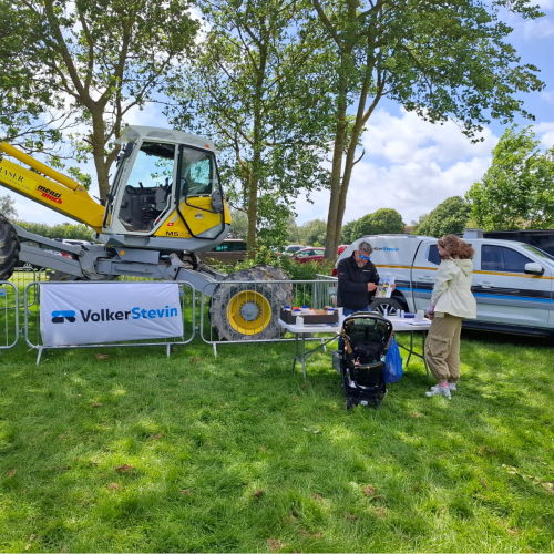 People in a field stood in front of a spider excavator. 