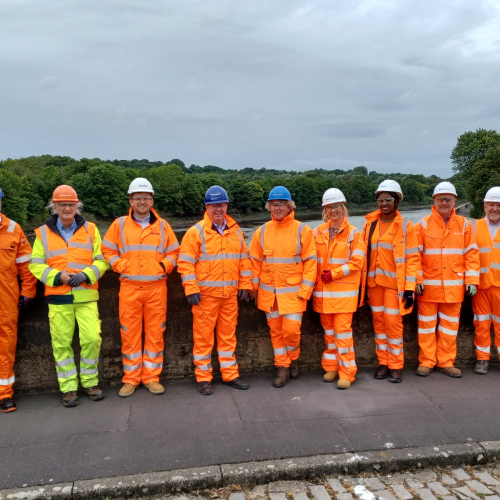 Group picture of men and women with some in orange hi-vis wear against a wall