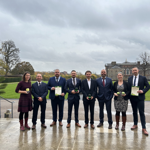 A group of eight men and women holding two certificates and two trophies