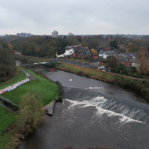 Picture of a helicopter carrying a bulk bag over a river.