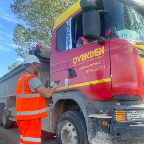 Picture of a man stood near a lorry on his phone.