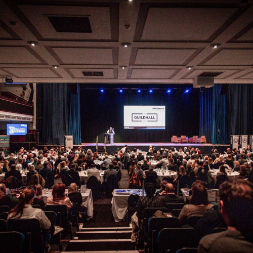an auditorium filled with people facing a stage with a large screen on the stage