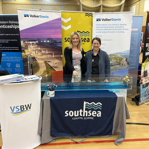 Two women stood behind a table with banners behind them 