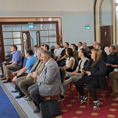 Room of people sat being presented to with slides on a  large screen