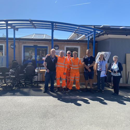 Group of men and women stood outside a school with furniture with bright blue skies