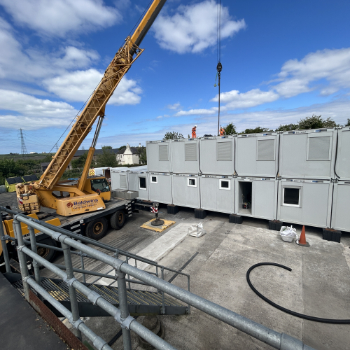 a crane putting into place double stacked accommodation units on a construction site