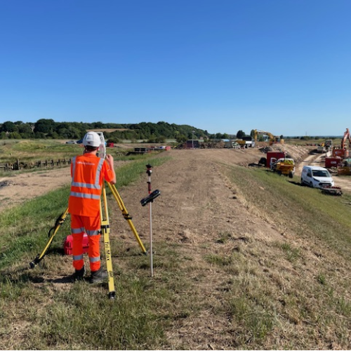 Construction worker in orange hi-vis workwear stood on a field operating equipment