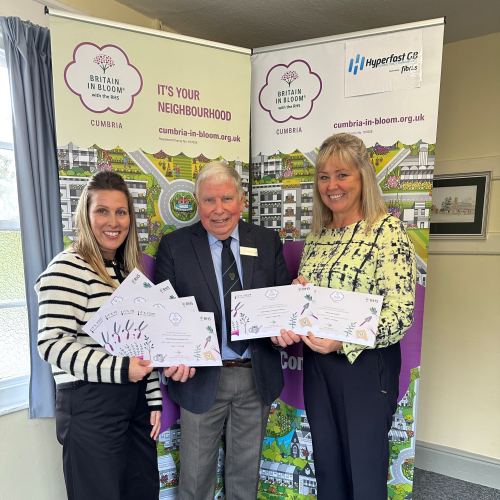 man in suit presenting certificates to two women stood in front of two pull up banners