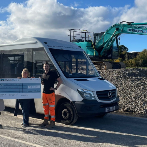 People with a giant check stood in front of a bus.