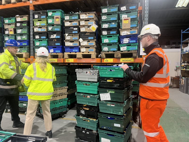 Two men and one women in orange and yellow hi vis in a warehouse stocking crates of food