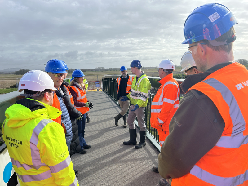 Group of men and women in hi-vis workwear stood on a bridge 