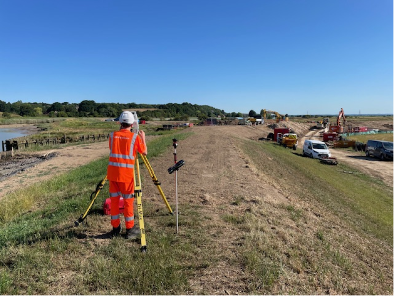 Construction worker in orange hi-vis workwear stood on a field operating equipment