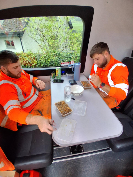 Two men sat at a table in hi-vis workwear eating a meal