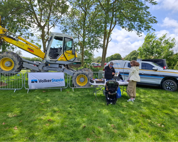 People in a field stood in front of a spider excavator. 