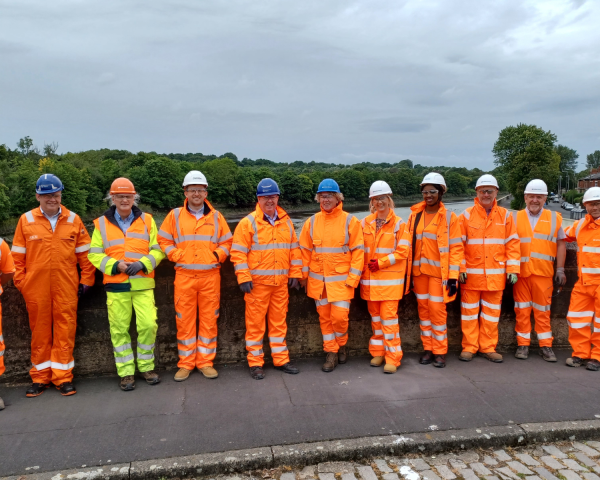 Group picture of men and women with some in orange hi-vis wear against a wall
