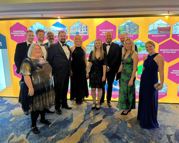 Group photo of men and women stood in front of a yellow backdrop with pink hexagons with images and text in