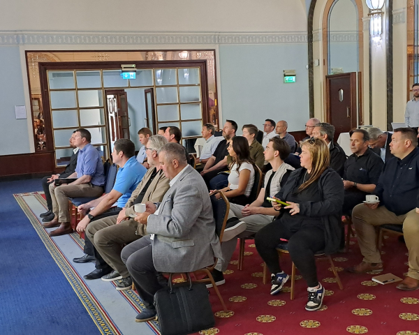 Room of people sat being presented to with slides on a  large screen