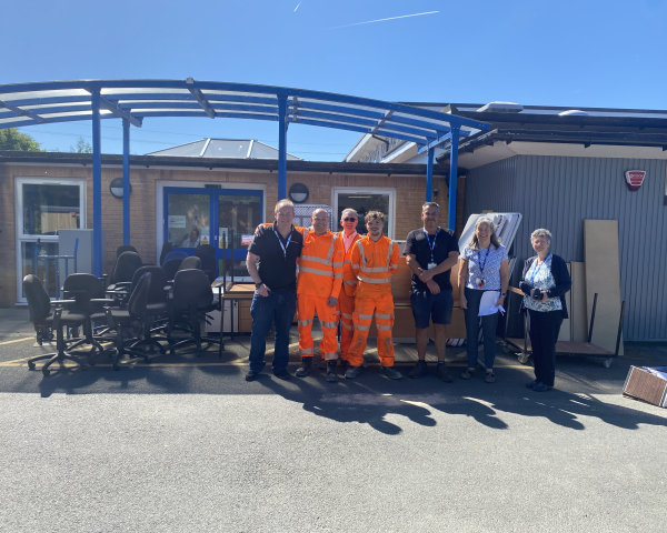 Group of men and women stood outside a school with furniture with bright blue skies