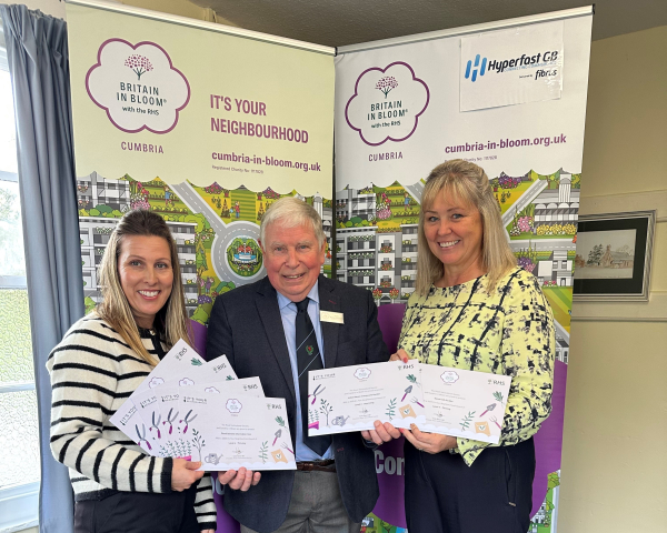 man in suit presenting certificates to two women stood in front of two pull up banners
