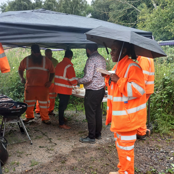 People in orange high vis cooking a BBQ outside in the rain.