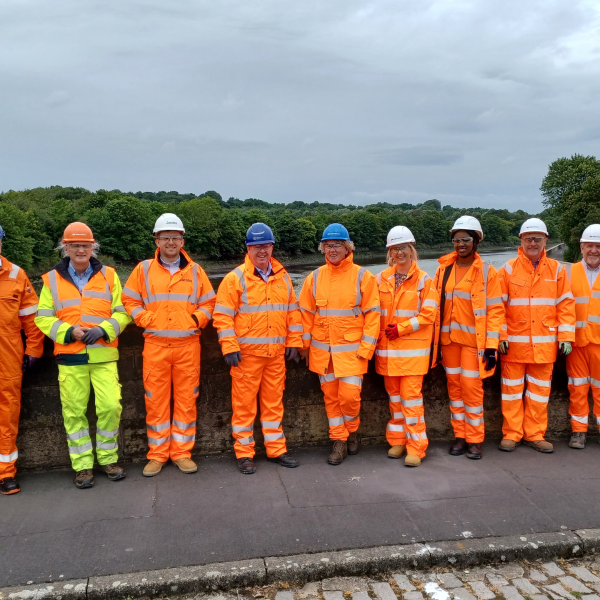 Group picture of men and women with some in orange hi-vis wear against a wall
