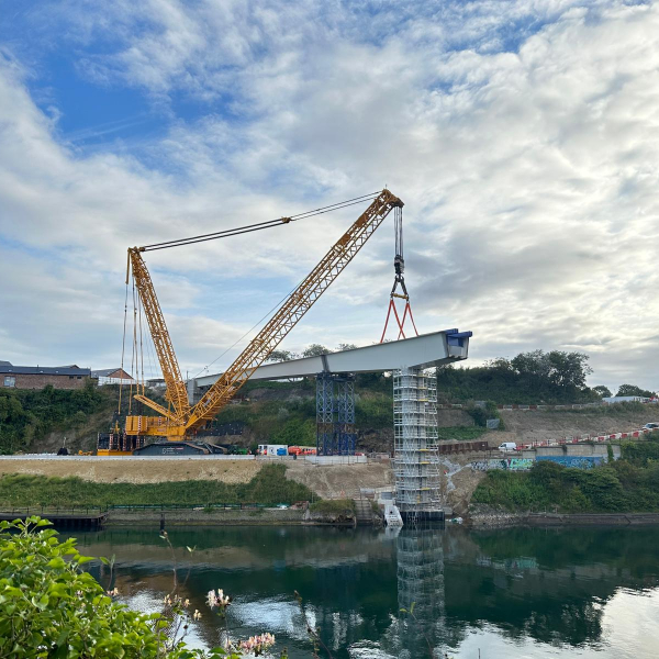 Crane lifting a section of the bridge into place on a sunny day.