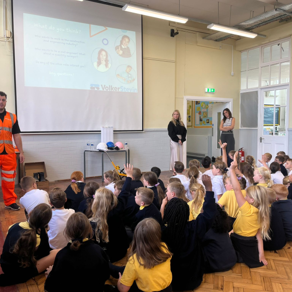 Man in hi-vis orange workwear stood in classroom presenting to children sat down on floor