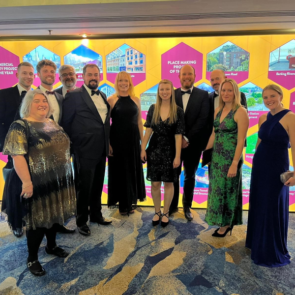 Group photo of men and women stood in front of a yellow backdrop with pink hexagons with images and text in