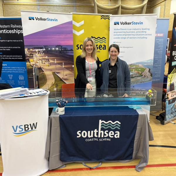 Two women stood behind a table with banners behind them 