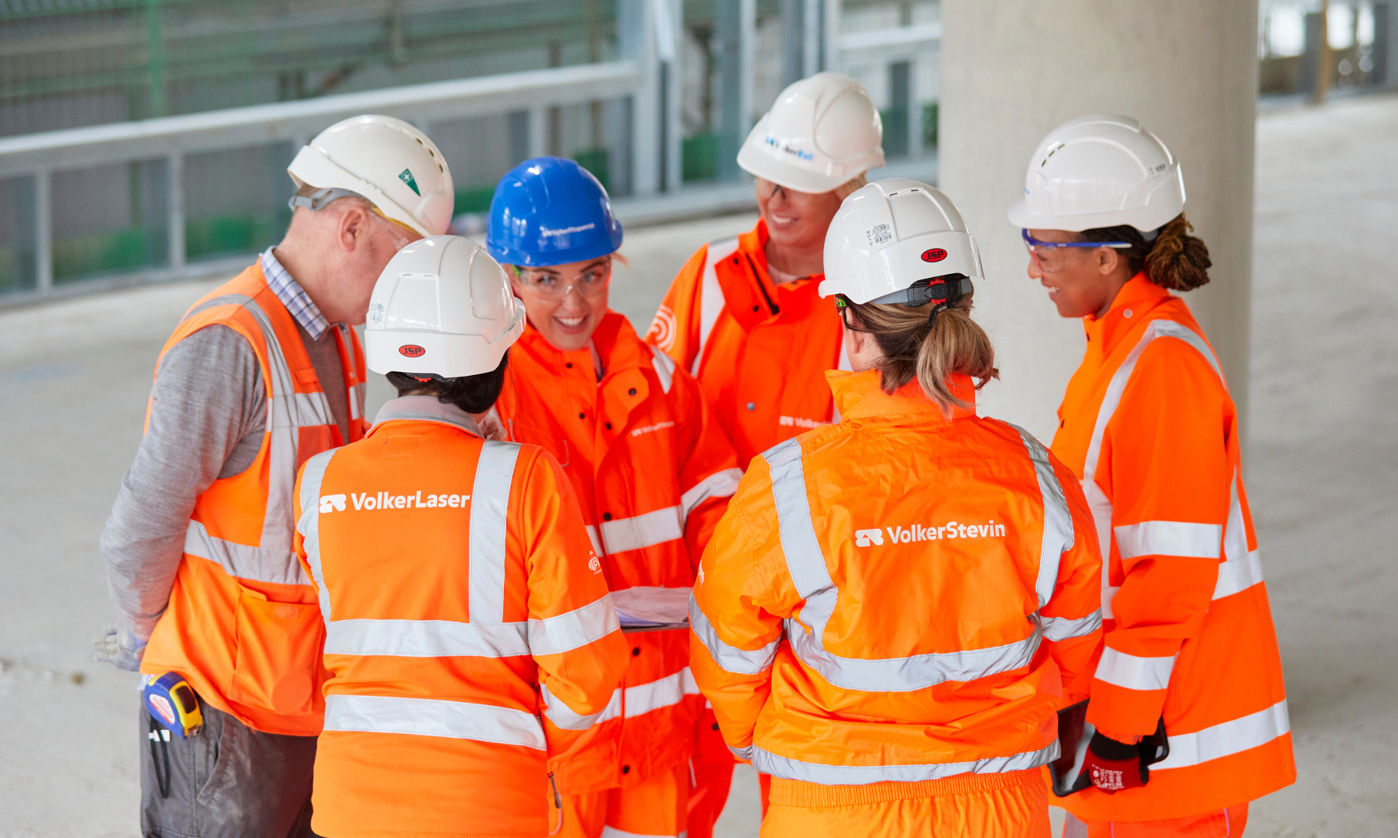 Group of six people all wearing orange PPE, stood talking/looking at each other