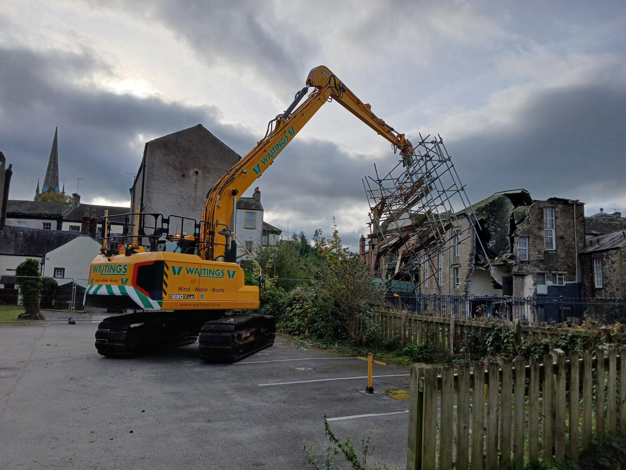 excavator by a river bank pulling out a large piece of scaffold