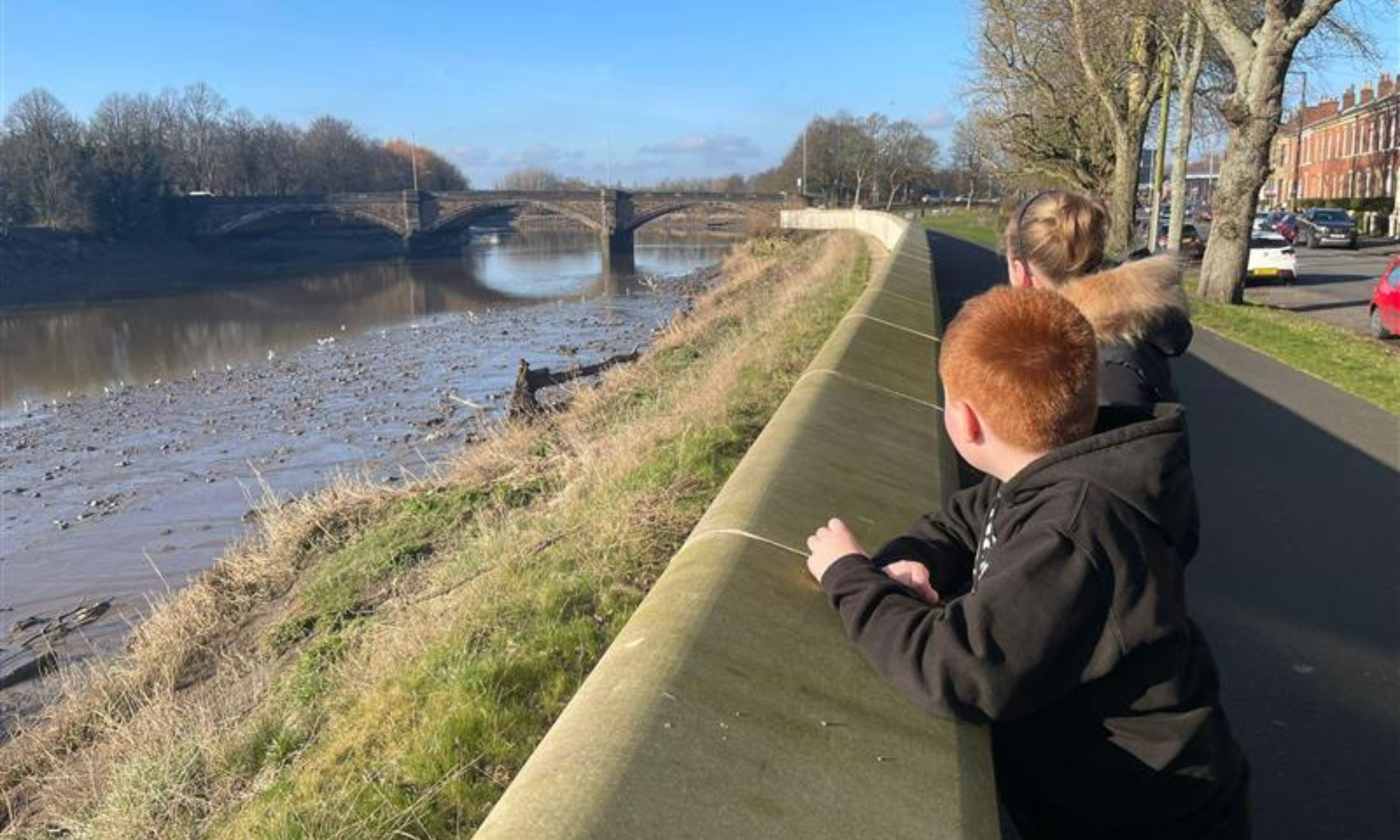 Two young boys look over a bridge at a river.