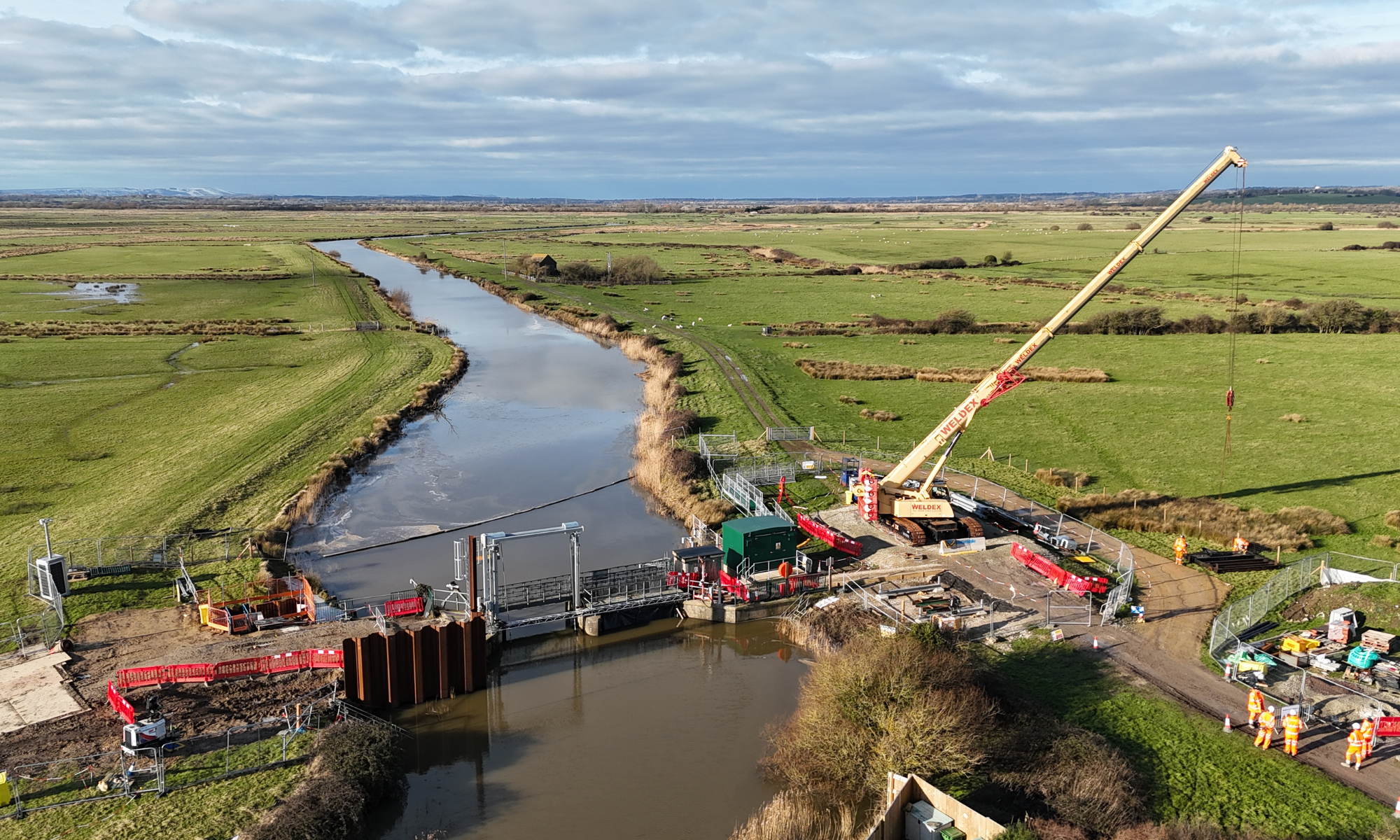 Aerial view of work across a river with a red and yellow crane