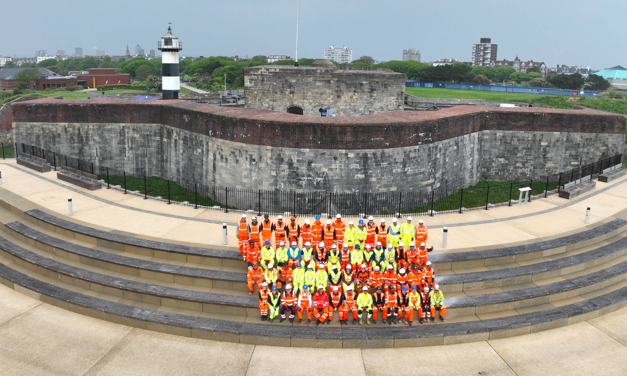 Group of men and women in hi-vis orange and yellow workwear stood on steps in front of Southsea Castle