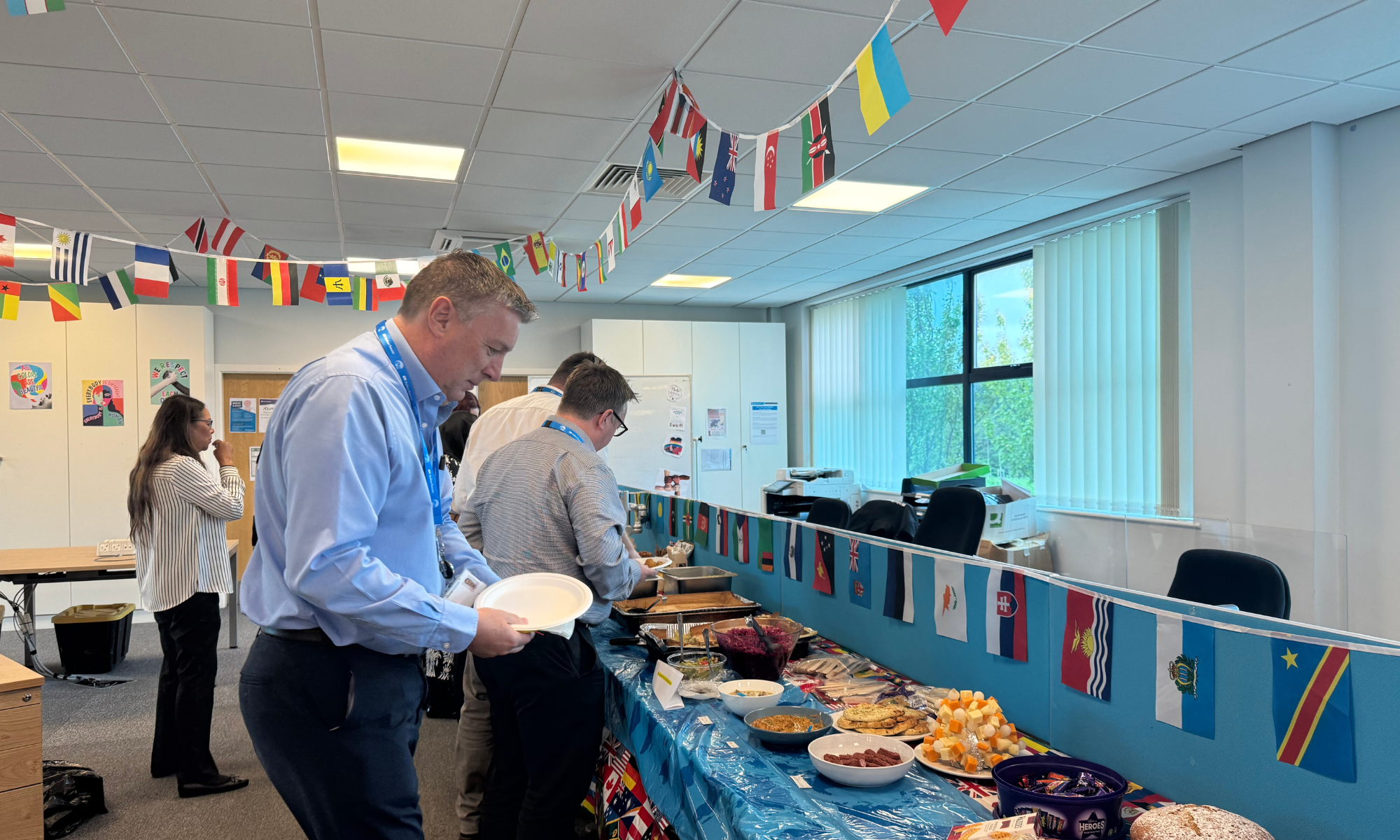 Men and women stood at a buffet in an office with flags of countries hung above
